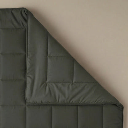De Zelesta Pure Uni Dekbed Katoen in olijfzwart wordt getoond op een beige oppervlak, met een hoek omgevouwen om de gewatteerde stiksels en textuur te benadrukken voor een ademend slaapcomfort.