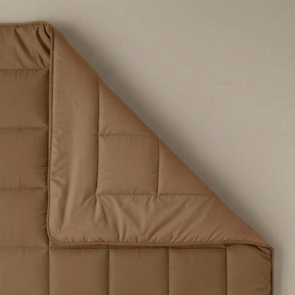 De Zelesta Pure Uni Dekbed Katoen - Cacao Bruin is netjes in één hoek gevouwen op een effen oppervlak en biedt een ademend slaapcomfort voor een rustgevende nacht.