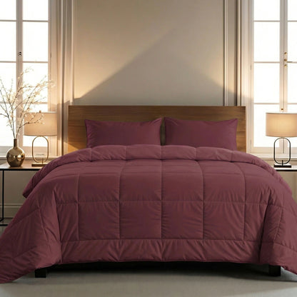 Een keurig opgemaakt bed met een Zelesta Pure Uni Dekbed Katoen in bordeaux rood en bijpassende kussens, geflankeerd door twee nachtkastjes met lampen en decoratieve takken, tegen een neutrale muur met twee ramen voor ademend slaapcomfort.