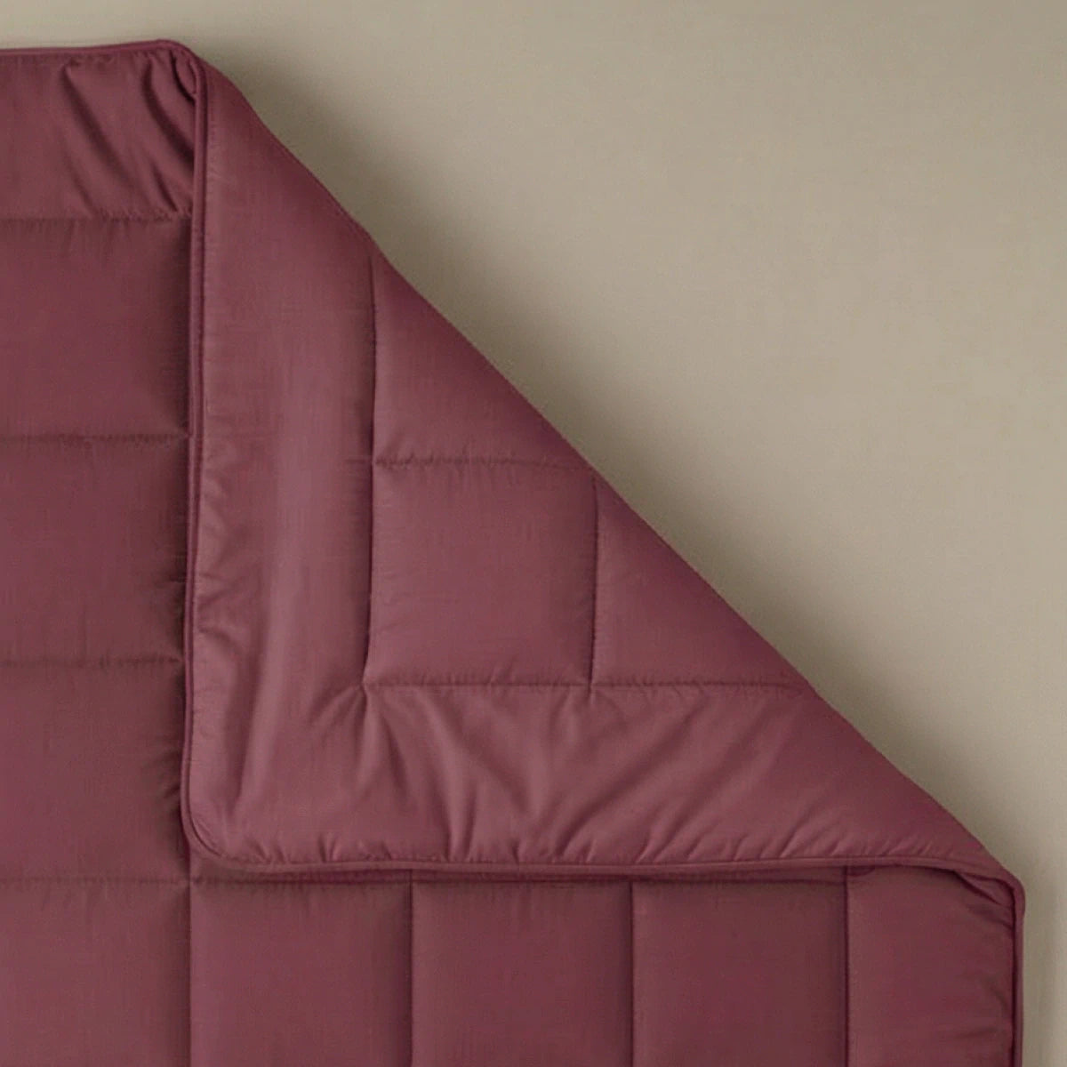 De Zelesta Pure Uni Dekbed Katoen in bordeaux rood is netjes gevouwen in één hoek tegen een beige achtergrond en biedt een ademend slaapcomfort.