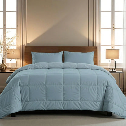 Een keurig opgemaakt bed met het Zelesta Pure Uni Dekbed Katoen in Sereen Blauw met bijpassende kussens, naast tafeltjes met lampjes, een houten hoofdeinde en twee hoge ramen voor ademend slaapcomfort.