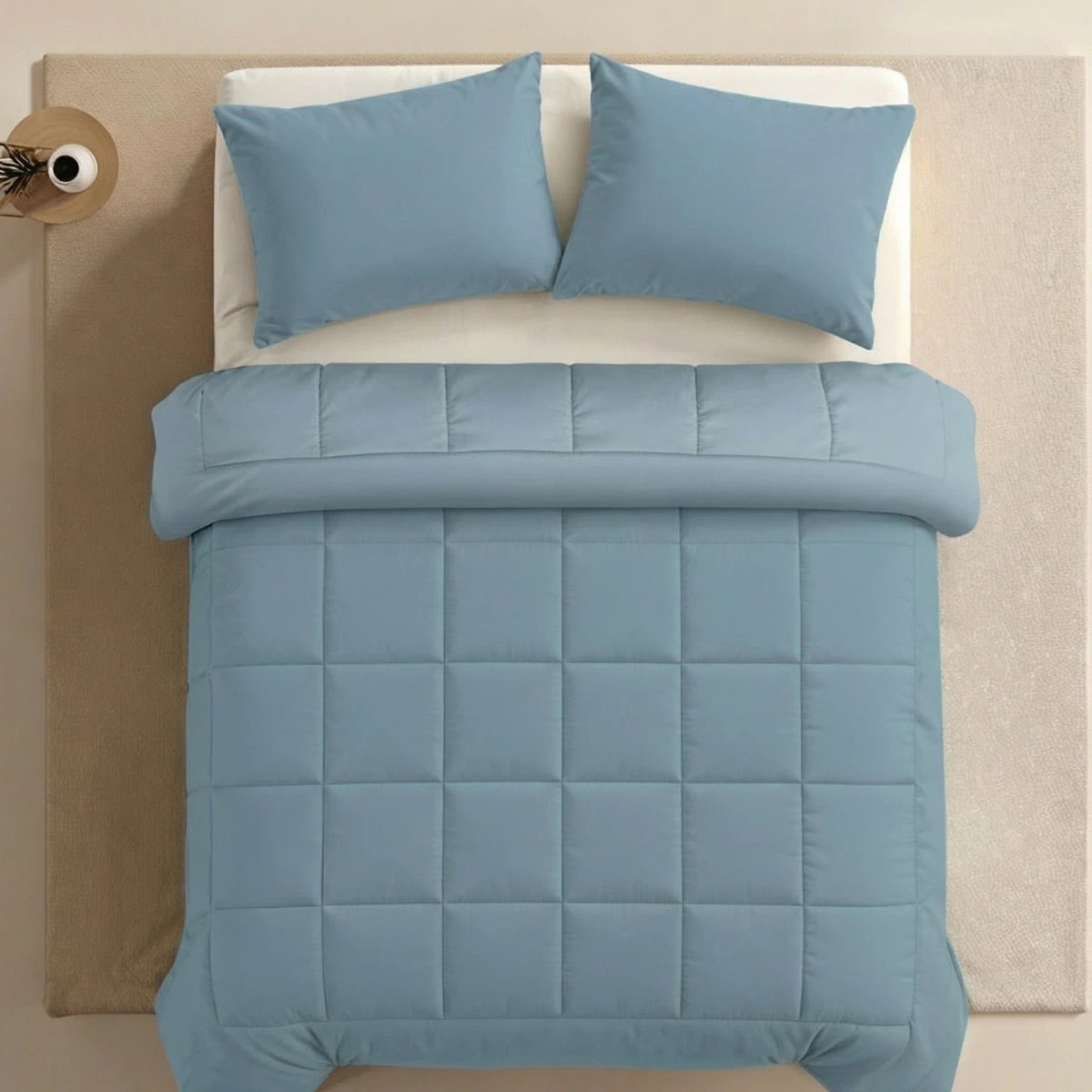 Een keurig opgemaakt bed met de Zelesta Pure Uni Dekbed Katoen in Sereen Blauw en twee bijpassende kussens, van bovenaf gezien op een beige vloerkleed, biedt een ademend slaapcomfort - perfect voor rustgevende nachten met duurzame dekbedden.