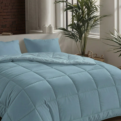 Een netjes opgemaakt bed met de Zelesta Pure Uni Dekbed Katoen in sereen blauw en twee bijpassende kussens, geplaatst bij grote ramen en kamerplanten voor een ademend slaapcomfort in een moderne slaapkamer.