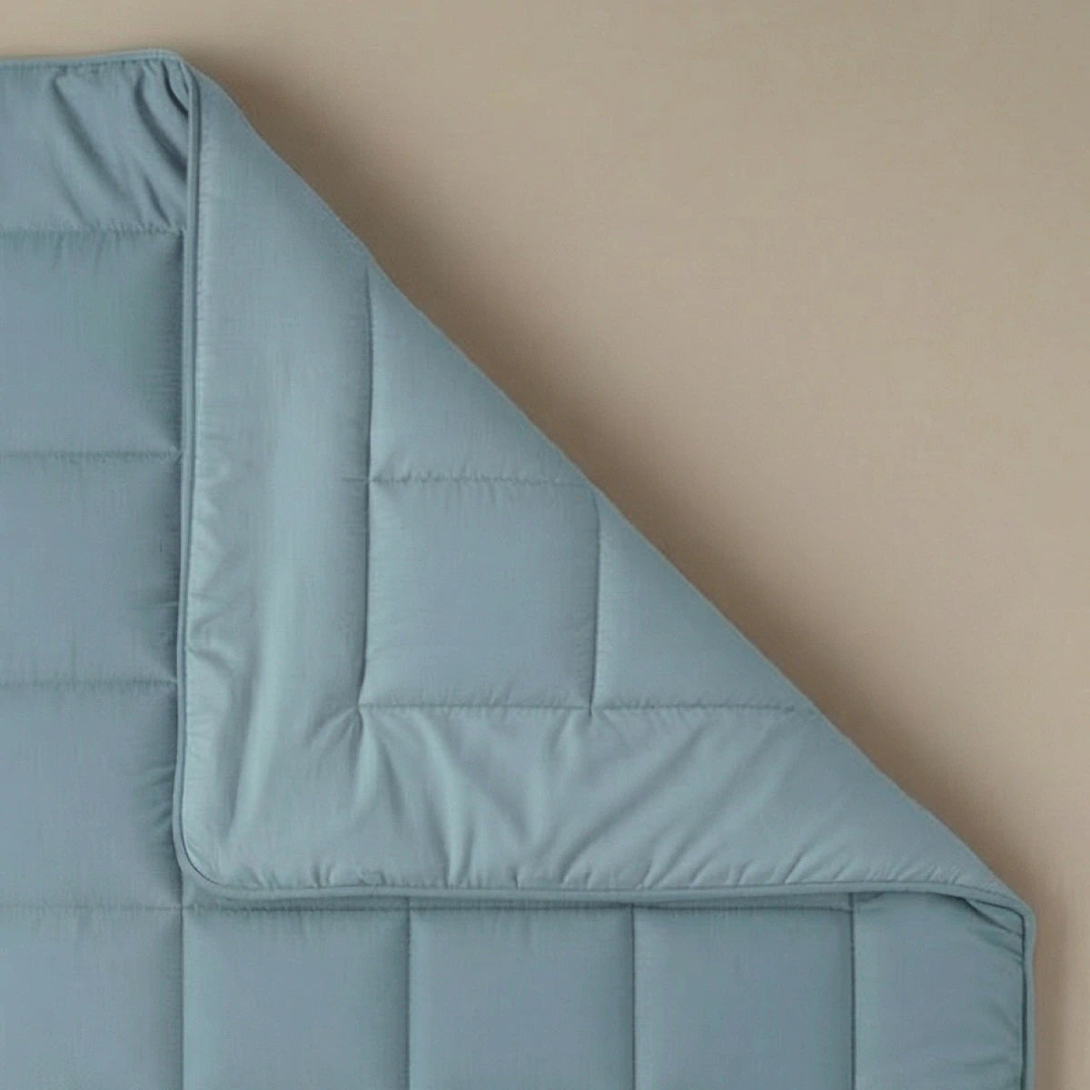 De Zelesta Pure Uni Dekbed Katoen in Sereen Blauw is netjes gevouwen over een beige oppervlak, laat de vierkante stiksels zien en biedt een ademend slaapcomfort.