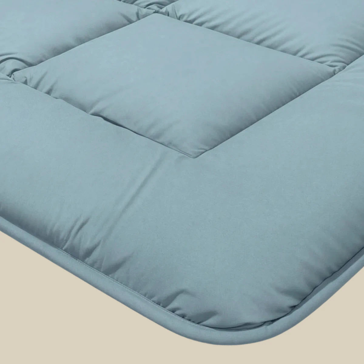 Close-up van een lichtblauw, gewatteerd stoffen kussen met vierkante stiksels voor ademend slaapcomfort - perfect om te combineren met de Zelesta Pure Uni Dekbed Katoen in sereen blauw of je favoriete dekbed.