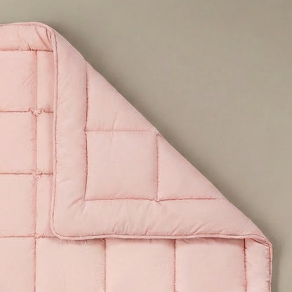 De Zelesta Pure Uni Dekbed Katoen in zacht roze is plat neergelegd op een beige ondergrond met een hoek omgeslagen, waardoor het doorgestikte stiksel wordt benadrukt voor een ademend slaapcomfort.