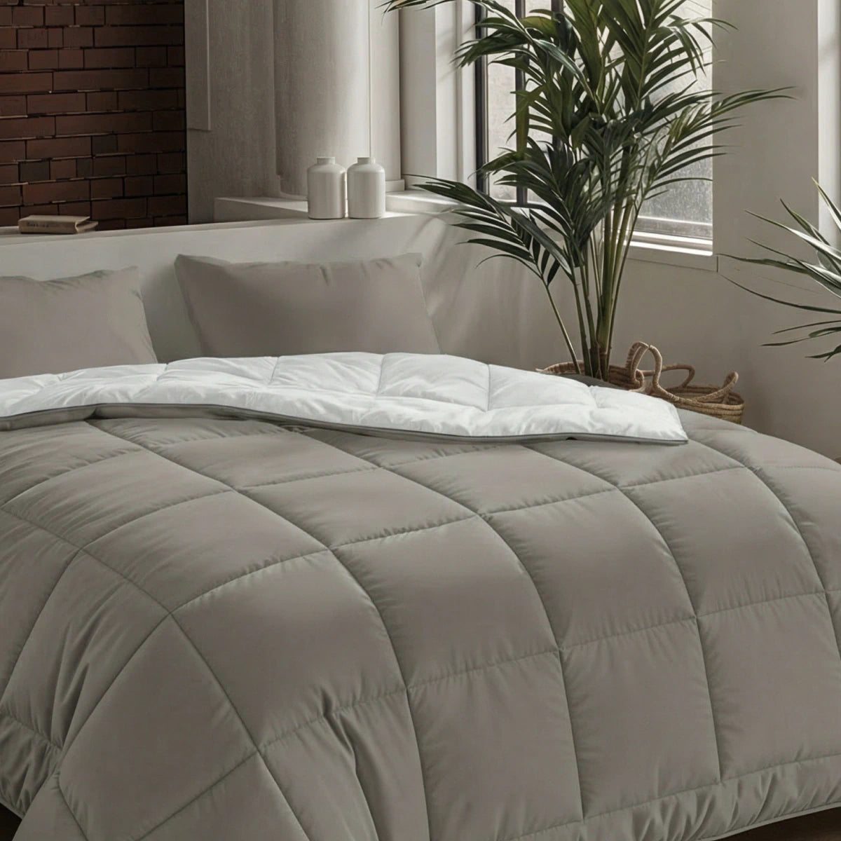 Een netjes opgemaakt bed met de Zelesta Pure Uni Dekbed Katoen - Antraciet Grijs, witte lakens, twee kussens en een plant bij het raam in een moderne, minimalistische slaapkamer voor ademend slaapcomfort.
