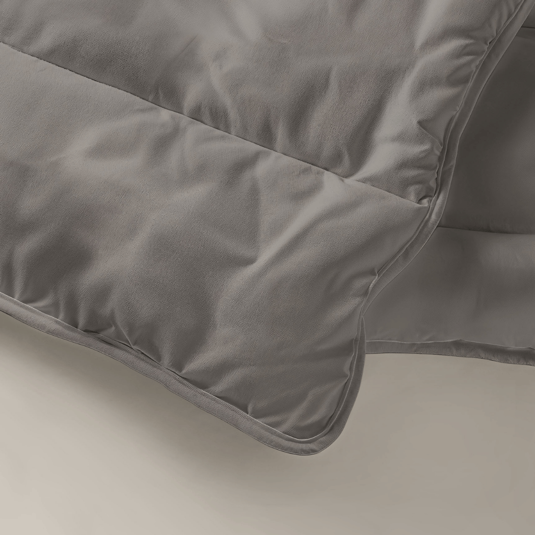 Een close-up van het Tender Grey Zelesta Royalbed benadrukt de gladde gewatteerde stof en de gedetailleerde stiksels - perfect als dekbed en overtrek in één.
