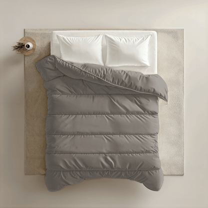Bovenaanzicht van een netjes opgemaakt bed met het Zelesta Royalbed - Tender Grey met twee witte kussens, een grijs dekbed en een beige vloerkleed, naast een rond houten nachtkastje met daarop een decoratief item.