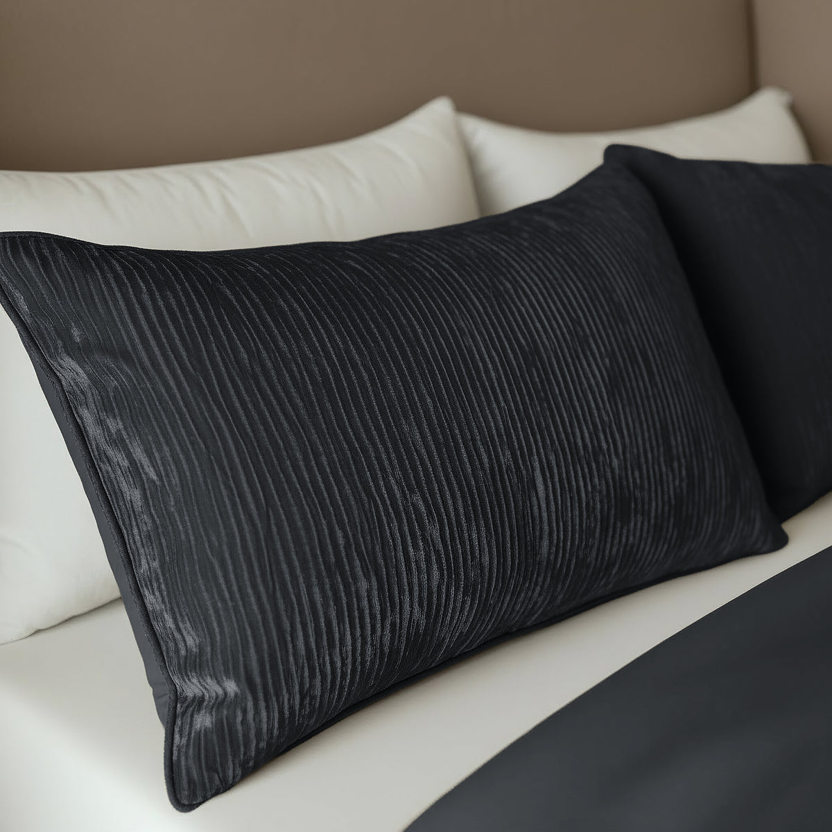 Twee antracietkleurige Zelesta Velvetbed Chique kussenslopen (set van 2) met geribbelde textuur en 100% polyester materiaal voegen comfort en stijl toe aan een netjes opgemaakt bed met donker beddengoed, afgezet tegen witte kussens.