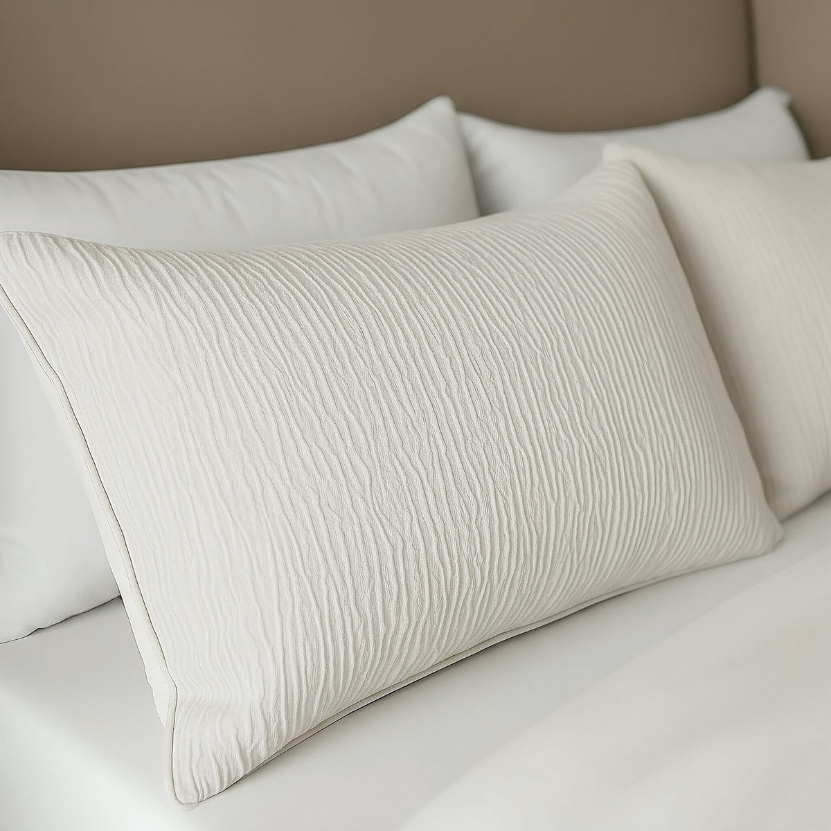 Close-up van een netjes opgemaakt bed met witte structuurkussens en frisse lakens tegen een beige hoofdeinde, met het Zelesta Velvetbed Chique Kussensloop Set van 2 - Beige voor extra comfort.