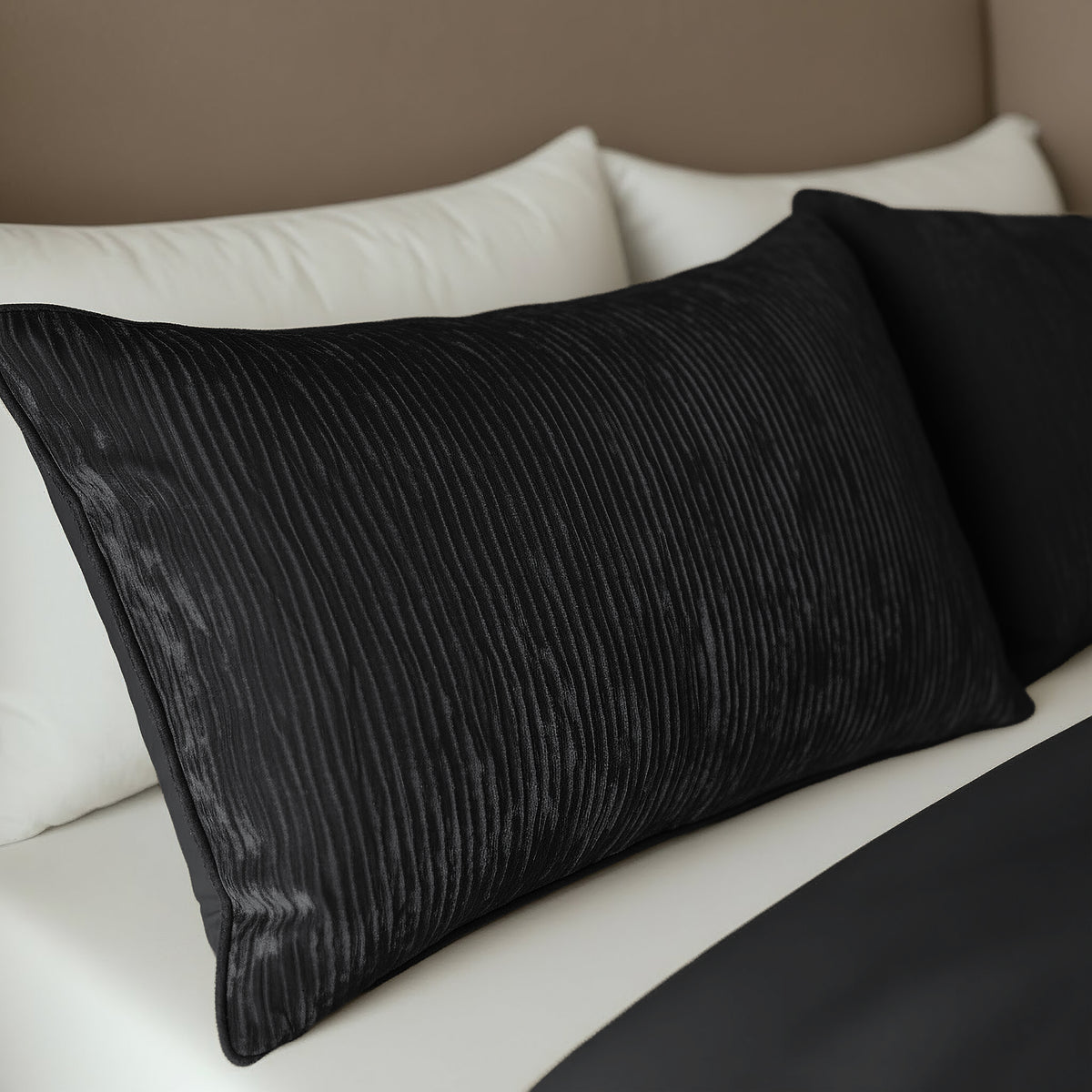 Twee Zelesta Velvetbed Chique Kussenslopen in zwart rusten op witte kussens bovenop een netjes opgemaakt bed met een zwart laken en beige hoofdeinde. Deze onderhoudsvriendelijke hoezen zijn gemaakt van 100% polyester en bieden een stijlvolle, gemakkelijke verzorging.