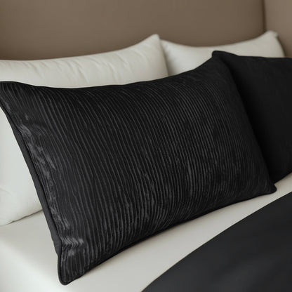 Twee Zelesta Velvetbed Chique Kussenslopen in zwart rusten op witte kussens bovenop een netjes opgemaakt bed met een zwart laken en beige hoofdeinde. Deze onderhoudsvriendelijke hoezen zijn gemaakt van 100% polyester en bieden een stijlvolle, gemakkelijke verzorging.