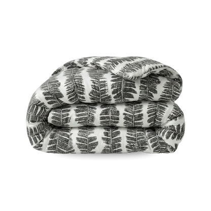Een opgevouwen Zelesta Wonderbed - Savanna Feather dekbed, met een zwart-wit varenbladmotief op wit, wordt getoond tegen een effen witte achtergrond en brengt hotelbeleving slaapkamer in huis.