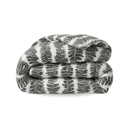Een opgevouwen Zelesta Wonderbed - Savanna Feather dekbed, met een zwart-wit varenbladmotief op wit, wordt getoond tegen een effen witte achtergrond en brengt hotelbeleving slaapkamer in huis.
