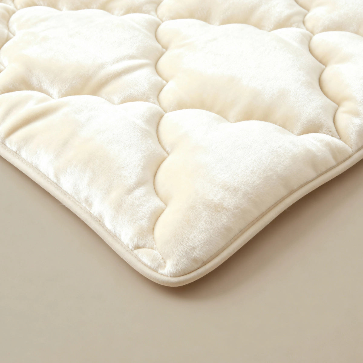 Een close-up van de Zelesta Flanel Uni - Beige, een pluche crèmekleurig flanellen dekbed of matrasonderlegger met een geschulpt, wolkachtig patroon op een beige oppervlak.