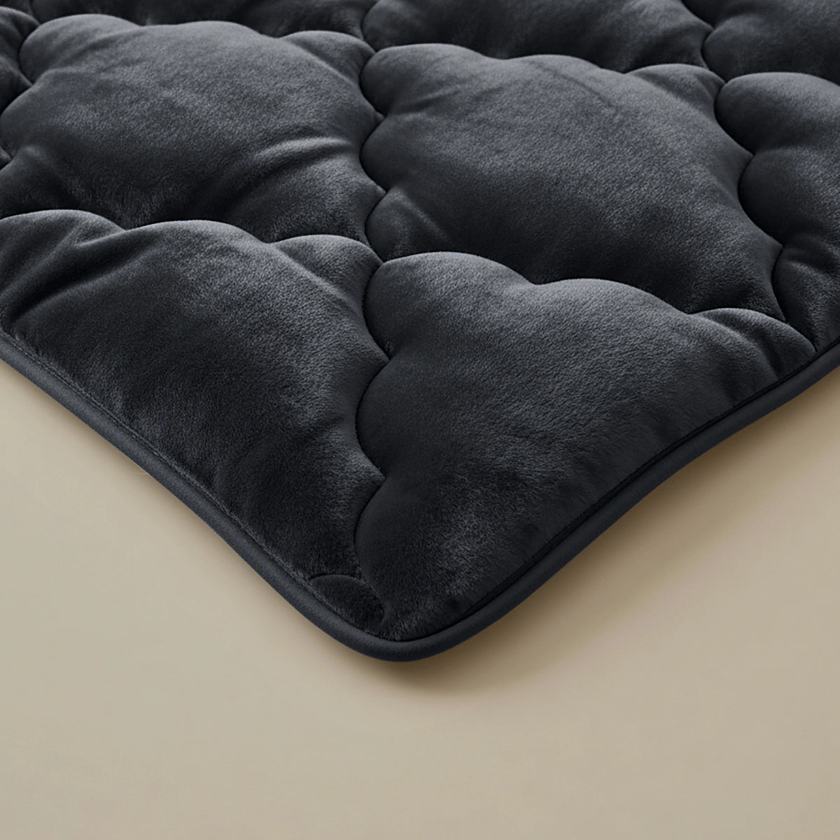 Een close-up van de Zelesta Flanel Uni - Zwart, een pluche zwart gewatteerd 2-in-1 dekbed of matras topper met een zachte fluweelachtige textuur en temperatuurregulerende eigenschappen, getoond op een lichtgekleurd oppervlak.