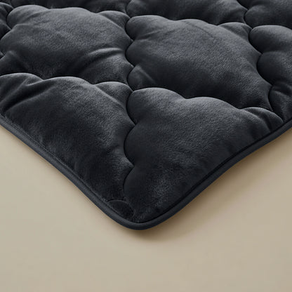 Een close-up van de Zelesta Flanel Uni - Zwart, een pluche zwart gewatteerd 2-in-1 dekbed of matras topper met een zachte fluweelachtige textuur en temperatuurregulerende eigenschappen, getoond op een lichtgekleurd oppervlak.