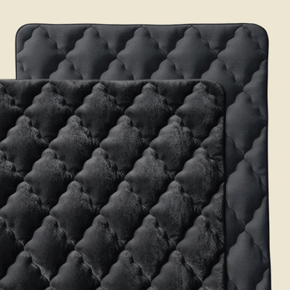 Twee zwarte Zelesta Flanel Uni - Zwart gewatteerde matten met afgeronde hoeken overlappen elkaar, met een pluche flanellen textuur aan de bovenkant en een gladde, temperatuurregulerende onderkant, tegen een lichtbeige achtergrond.