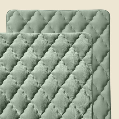 Twee doorgestikte, groene badmatten met een ruitpatroon zijn gestapeld op een beige achtergrond - perfect om te combineren met het Zelesta Flanel Uni - Donker Groen dekbed voor gezellig, gecoördineerd comfort in huis.