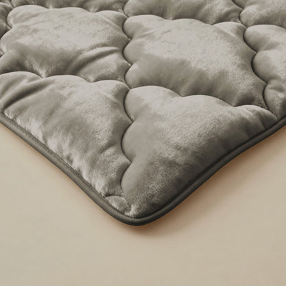 Een close-up van de Zelesta Flanel Uni - Taupe toont de zachte, taupe, gewatteerde textuur en het pluche materiaal - vergelijkbaar met een temperatuurregulerend 2-in-1 dekbed - rustend op een beige oppervlak met een lichte glans en zacht gewatteerde delen.