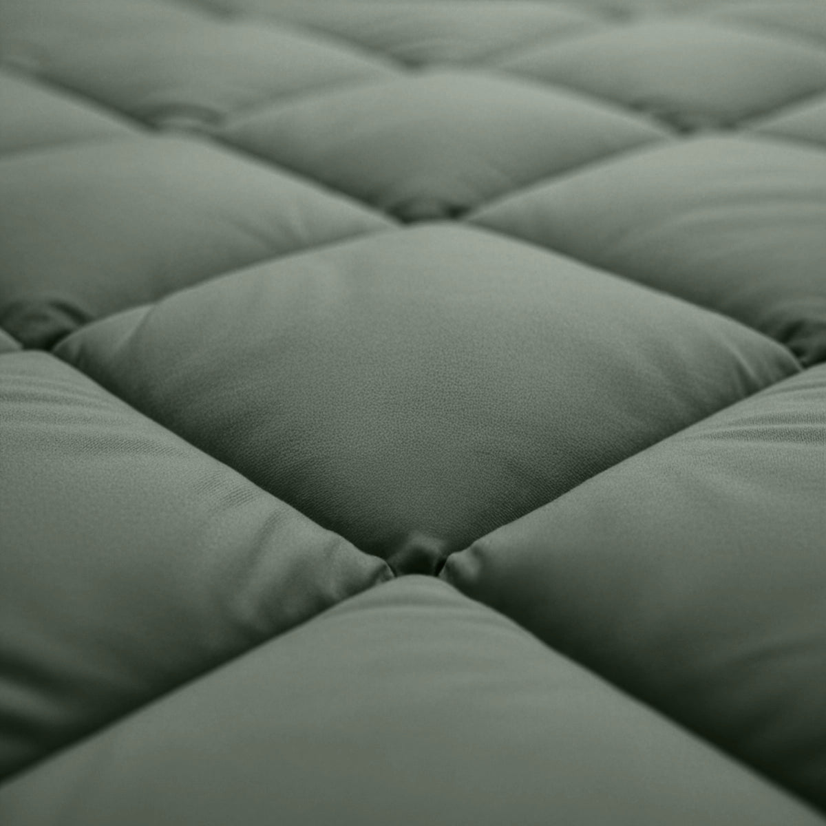 Close-up van het Zelesta Comfort Uni diamond Dekbed - Groen, met het groen gewatteerde oppervlak met vierkante gewatteerde delen en zichtbare stiksels, dat doet denken aan klassieke dekbedden voor gebruik met een vaste overtrek.