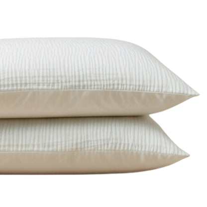 Het Zelesta Velvetbed Chique Kussensloop Set van 2 in beige, gemaakt van 100% polyester, heeft subtiele strepen - perfect voor een comfortabel nachtrust. Twee crèmekleurige kussenslopen zijn gestapeld tegen een witte achtergrond.