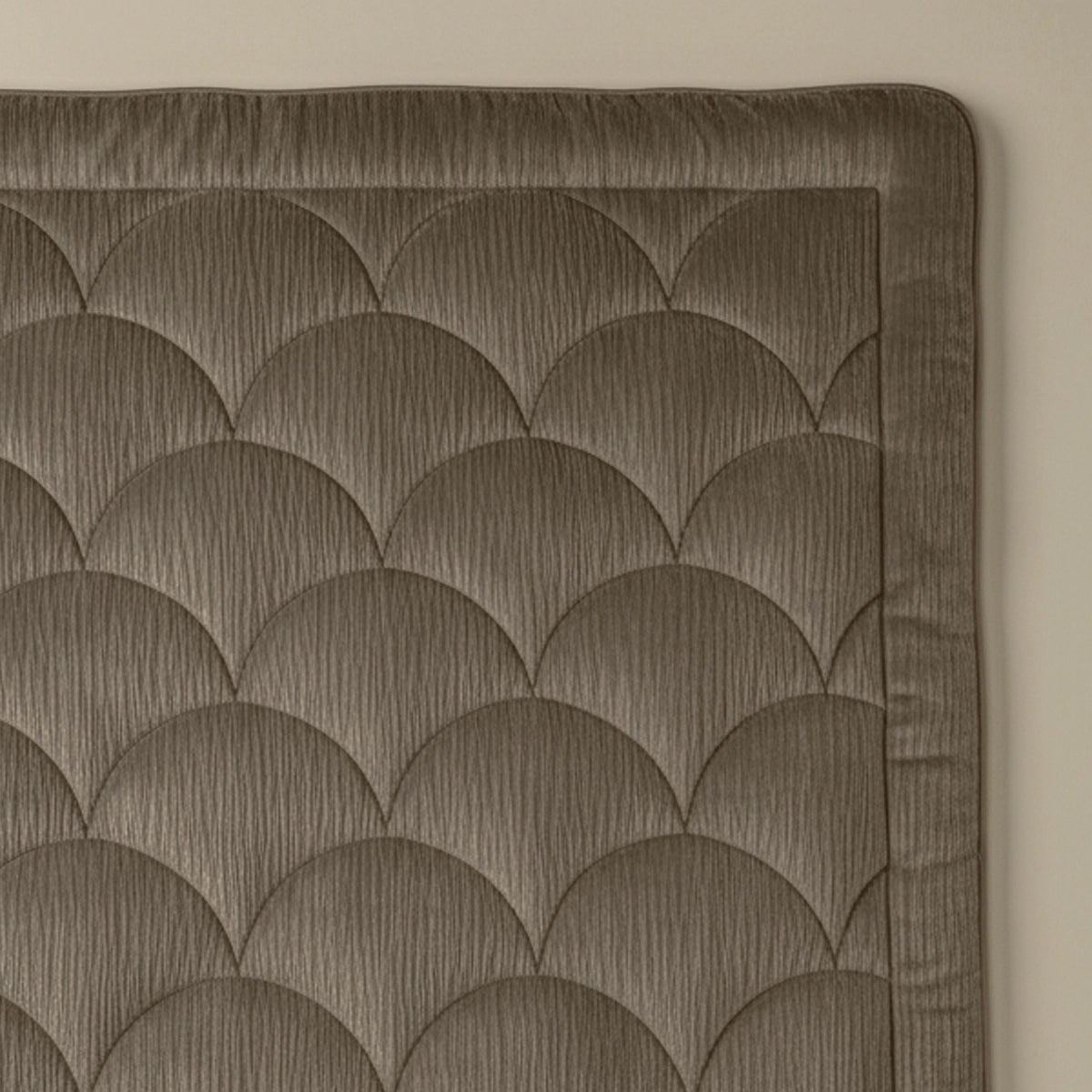Een close-up van gewatteerde stof met een schulppatroon en gestikte rand. Het Zelesta Flanel Velvetbed Chique - Taupe voegt een luxe uitstraling toe aan elke slaapkamer.
