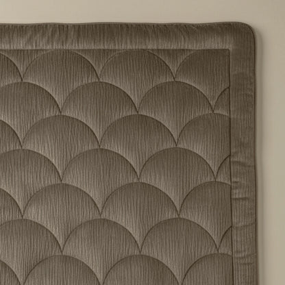 Een close-up van gewatteerde stof met een schulppatroon en gestikte rand. Het Zelesta Flanel Velvetbed Chique - Taupe voegt een luxe uitstraling toe aan elke slaapkamer.