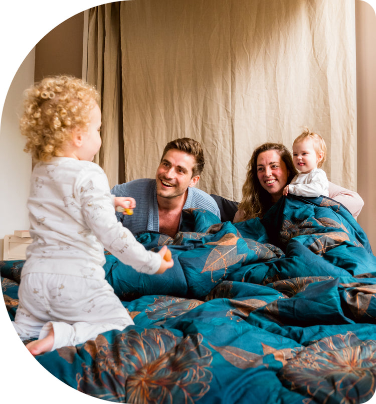 Familie speelt vrolijk in bed onder een blauwgroen Zelesta dekbed met botanische print