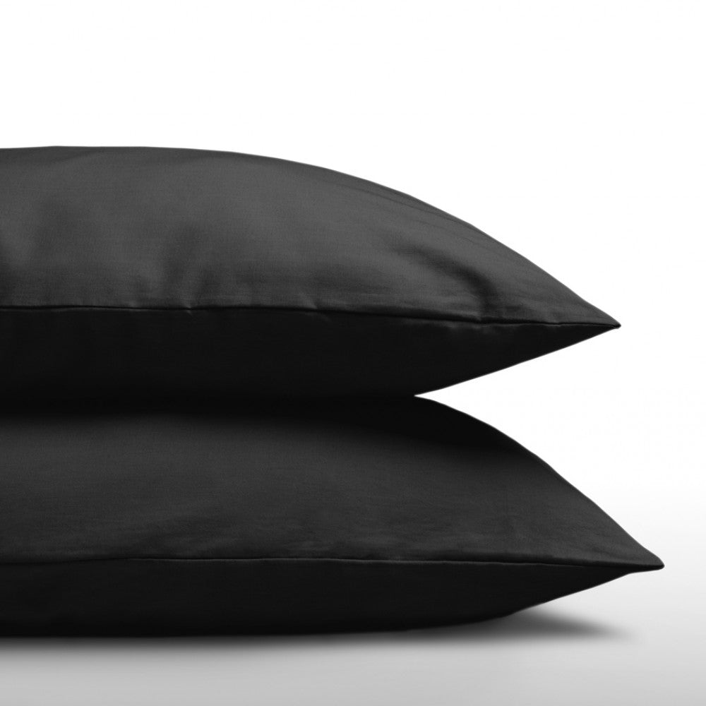 Two zwart Katoenen Kussenslopen zijn op elkaar gestapeld tegen een witte achtergrond, met een luxe uitstraling en gemaakt van 100% zacht katoen voor ultiem comfort.